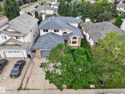 Pitched shingle roof, two-car garage, arched entry window, brick facade accents, mature trees - 