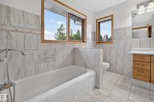 Bathroom featuring wood-frame windows, tiled walls with decorative band, a white bathtub, and a wood vanity with a white countertop - 306 Twin Brooks Drive Nw, Edmonton, AB 