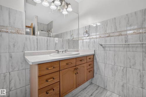 Bathroom featuring a wood-finish vanity with a built-in sink, a light-toned countertop, and a large wall-mounted mirror - 306 Twin Brooks Drive Nw, Edmonton, AB 