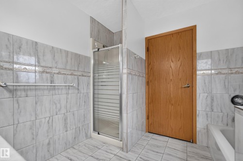 Tiled shower with glass enclosure, wood-finish door, and integrated bathtub - 306 Twin Brooks Drive Nw, Edmonton, AB 