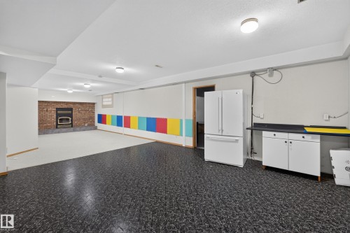 Spacious lower-level room featuring a brick-surround fireplace, contrasting flooring, and built-in cabinetry with a countertop - 306 Twin Brooks Drive Nw, Edmonton, AB 