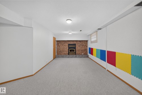 Spacious room featuring light-colored carpeting, a brick accent wall with a built-in fireplace, and overhead lighting - 306 Twin Brooks Drive Nw, Edmonton, AB 