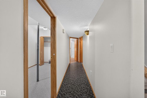 Hallway featuring patterned resilient flooring, light-toned wall paint, decorative wall sconces, and wood-finish door frames - 306 Twin Brooks Drive Nw, Edmonton, AB 