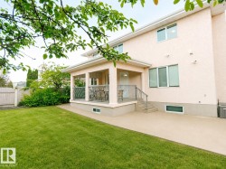Expansive lawn area, stucco exterior, covered patio with metal railings, hardscaped patio, and multiple windows - 