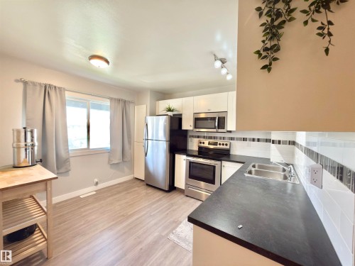 Kitchen featuring stainless steel appliances, white cabinetry, dark countertops, a white subway tile backsplash with accent tiling, and wood-finish flooring - #13 18010 98 Av Nw Nw, Edmonton, AB - Indoor Photo Showing Kitchen With Stainless Steel Kitchen With Double Sink