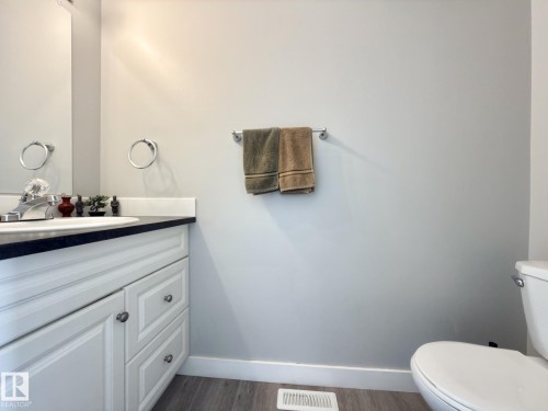 White vanity with paneled doors and drawers, dark countertop, and integrated sink - #13 18010 98 Av Nw Nw, Edmonton, AB - Indoor Photo Showing Bathroom