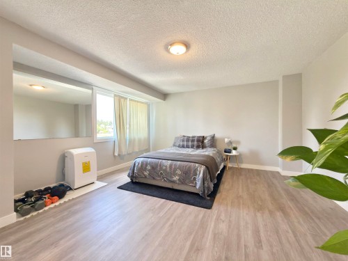 Wood-finish flooring, light grey wall paint, flush mount ceiling light, and a large window - #13 18010 98 Av Nw Nw, Edmonton, AB - Indoor Photo Showing Bedroom
