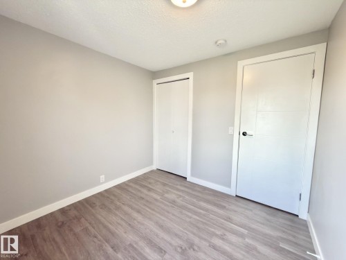 Wood-finish flooring, light grey wall paint, and white trim - #13 18010 98 Av Nw Nw, Edmonton, AB - Indoor Photo Showing Other Room