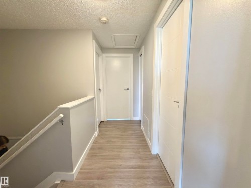 Wood-finish flooring, crisp white trim, and a contemporary railing design - #13 18010 98 Av Nw Nw, Edmonton, AB - Indoor Photo Showing Other Room
