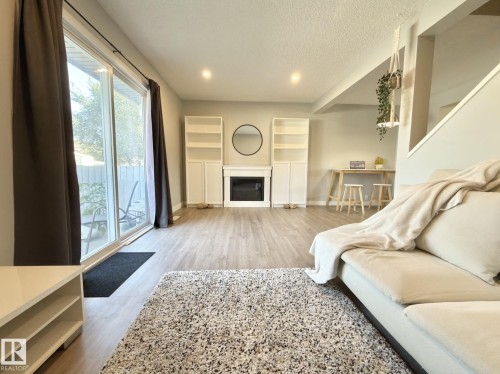 Spacious interior featuring wood-finish flooring, a built-in electric fireplace, sliding glass door access to the exterior, and recessed lighting - #13 18010 98 Av Nw Nw, Edmonton, AB - Indoor With Fireplace