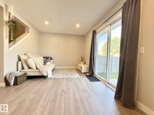 Wood-finish flooring throughout, recessed ceiling lighting, and a sliding glass door leading to the exterior - #13 18010 98 Av Nw Nw, Edmonton, AB - Indoor Photo Showing Other Room