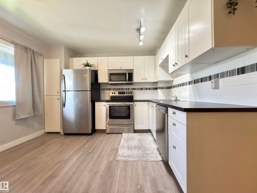 Kitchen featuring white cabinetry, dark countertops, a white subway tile backsplash with accent stripe, stainless steel appliances, and wood-finish flooring - #13 18010 98 Av Nw Nw, Edmonton, AB - Indoor Photo Showing Kitchen With Stainless Steel Kitchen