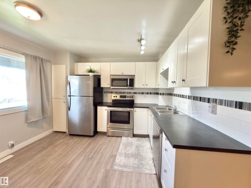 White cabinetry paired with stainless steel appliances, dark countertops, and wood-finish flooring - #13 18010 98 Av Nw Nw, Edmonton, AB - Indoor Photo Showing Kitchen With Stainless Steel Kitchen With Double Sink