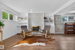 Wood-finish flooring, built-in shelving, stone-finish fireplace surround with a gold-tone trim, and white-framed windows - 