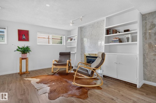 Wood-finish flooring, built-in shelving, integrated lower cabinetry, a fireplace with a stone-finish surround, and track lighting - 12 Latimer Place, St. Albert, AB - Indoor