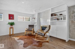 Wood-finish flooring, built-in shelving, integrated lower cabinetry, a fireplace with a stone-finish surround, and track lighting - 