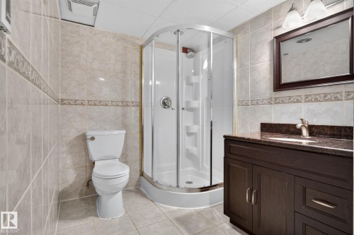 Tiled bathroom featuring a corner shower enclosure, dark wood-finish vanity with an undermount sink, and a framed mirror - 12 Latimer Place, St. Albert, AB - Indoor Photo Showing Bathroom