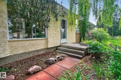 Textured stucco exterior, large picture window, multi-tiered concrete steps, vibrant green foliage, and mature trees - 