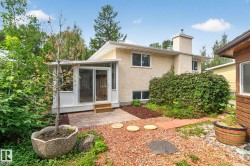 Rear exterior featuring a sunroom addition with sliding glass doors, a paver patio, and mature landscaping - 