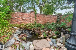 Brick privacy wall with integrated garden beds, rock-lined water feature, and mature plantings - 