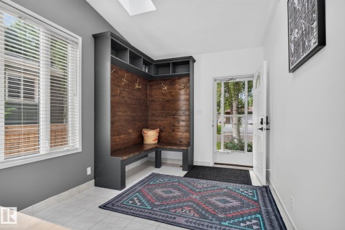 Built-in mudroom bench with wood-paneled backing and integrated shelving, white tile flooring, double-pane window with blinds, and a skylight - 12 Latimer Place, St. Albert, AB - Indoor Photo Showing Other Room