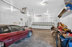 Garage featuring extensive built-in cabinetry, overhead lighting, garage door opener mechanism, and concrete flooring - 