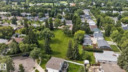 Expansive green space with mature trees, surrounded by residential properties, featuring a paved street and abundant foliage - 
