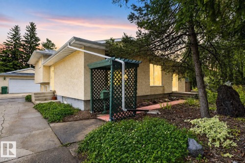 Stucco exterior finish, attached garage with white door, front entryway with concrete steps, front yard landscaping with mature trees, and a decorative trellis - 12 Latimer Place, St. Albert, AB - Outdoor
