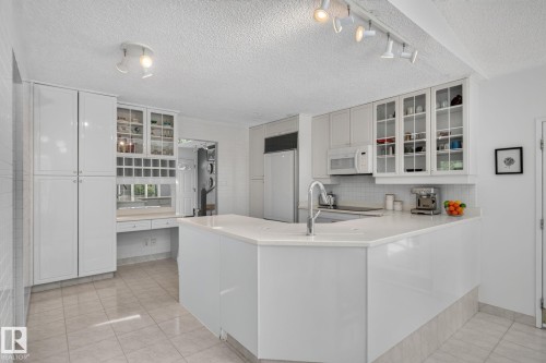 White kitchen with a peninsula, built-in desk, glass-front upper cabinetry, stainless steel sink, and tile flooring - 12 Latimer Place, St. Albert, AB - Indoor Photo Showing Kitchen