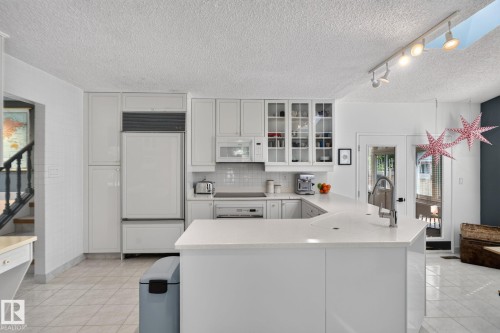 White kitchen cabinetry with glass-front display cabinets, white subway tile backsplash, white countertops, and integrated appliances - 12 Latimer Place, St. Albert, AB - Indoor Photo Showing Kitchen