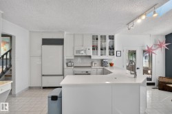 White kitchen cabinetry with glass-front display cabinets, white subway tile backsplash, white countertops, and integrated appliances - 