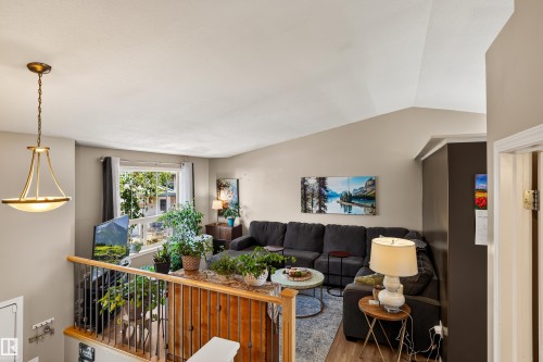 Vaulted ceiling living area featuring a large window, brass-finish chandelier, and wood-finish flooring - #9 6506 47 St, Cold Lake, AB - Indoor