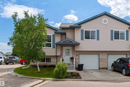 Siding exterior with blue decorative shutters, stone facade accents, and two attached garages - #9 6506 47 St, Cold Lake, AB - Outdoor With Facade