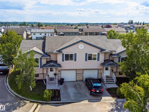 Dual garage doors, stone veneer accents, pitched roofline, mature landscaping, and an extended driveway - #9 6506 47 St, Cold Lake, AB - Outdoor With Facade