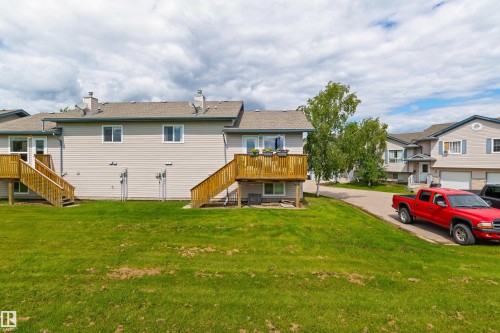 Rear exterior with two wood decks, light-colored horizontal siding, and a sloped grass lawn - #9 6506 47 St, Cold Lake, AB - Outdoor