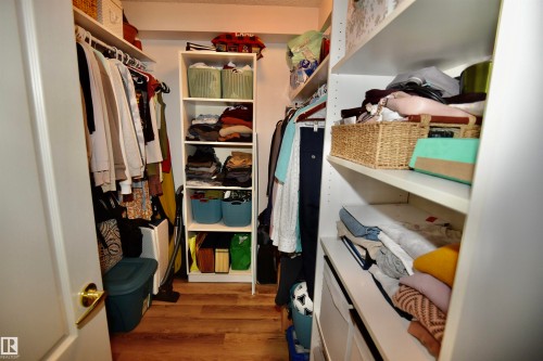 Walk-in closet featuring wood-finish flooring, white built-in shelving, white hanging rods, and a white interior door with brass hardware - #706 9741 110 St Nw, Edmonton, AB - Indoor With Storage