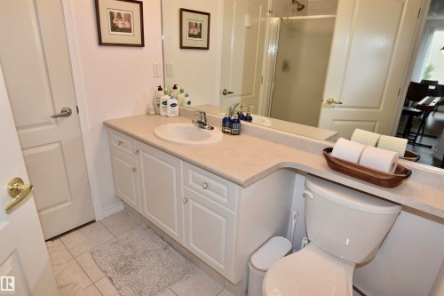 Dual-sink vanity with ample countertop space and white cabinetry storage, ceramic tile flooring, and large framed mirror - #706 9741 110 St Nw, Edmonton, AB - Indoor Photo Showing Bathroom