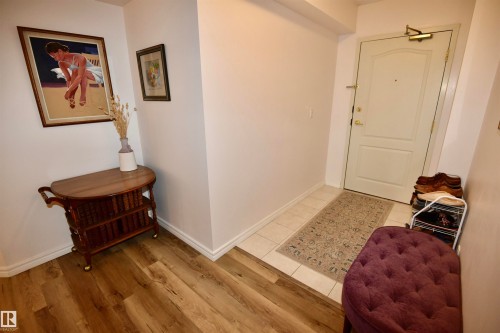 White entry door with polished hardware, contrasting light-tone tile flooring, and wood-finish flooring - #706 9741 110 St Nw, Edmonton, AB - Indoor Photo Showing Other Room