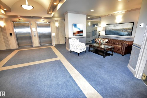 Lobby area featuring two stainless steel elevators, patterned blue carpeting with a light-colored inlay, and recessed lighting - #706 9741 110 St Nw, Edmonton, AB - Indoor Photo Showing Other Room