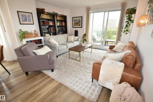 Spacious living area featuring wood-finish flooring, a full-height built-in bookshelf, and a sliding glass door leading to a private outdoor space - #706 9741 110 St Nw, Edmonton, AB - Indoor Photo Showing Living Room