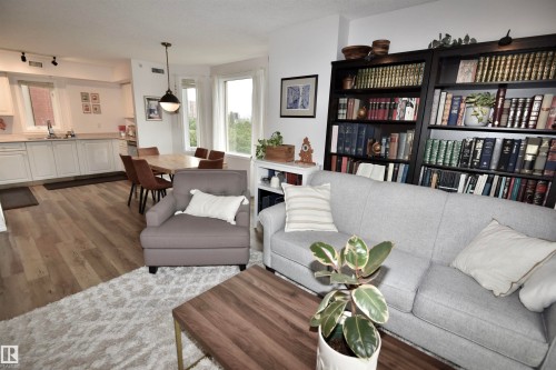 Open-concept living space with wood-finish flooring, white cabinetry, and abundant natural light from multiple windows - #706 9741 110 St Nw, Edmonton, AB - Indoor Photo Showing Living Room