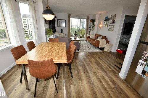 Expansive wood-finish flooring throughout, featuring a dining area with a butcher block style table, a modern pendant light fixture, and large windows - #706 9741 110 St Nw, Edmonton, AB - Indoor Photo Showing Dining Room