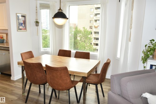 Dining area with wood-finish flooring, a contemporary pendant light fixture, and large windows - #706 9741 110 St Nw, Edmonton, AB - Indoor Photo Showing Dining Room