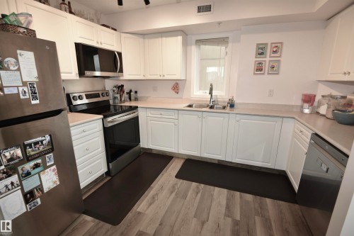 Kitchen featuring white cabinetry, light countertops, wood-finish flooring, stainless steel appliances, and a window above the sink - #706 9741 110 St Nw, Edmonton, AB - Indoor Photo Showing Kitchen With Double Sink