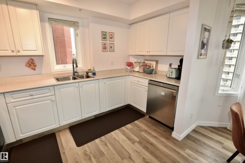 Kitchen featuring wood-finish flooring, white cabinetry, light-toned countertops, a stainless steel dishwasher, and a double basin sink with a gooseneck faucet - #706 9741 110 St Nw, Edmonton, AB - Indoor Photo Showing Kitchen With Double Sink