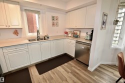 Kitchen featuring wood-finish flooring, white cabinetry, light-toned countertops, a stainless steel dishwasher, and a double basin sink with a gooseneck faucet - 