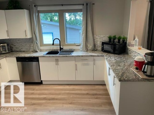 U-shaped kitchen featuring white cabinetry, light-toned countertops, a black sink with a matte black faucet, and a stainless steel dishwasher - 27 Gatewood Avenue, St. Albert, AB - Indoor Photo Showing Kitchen With Double Sink