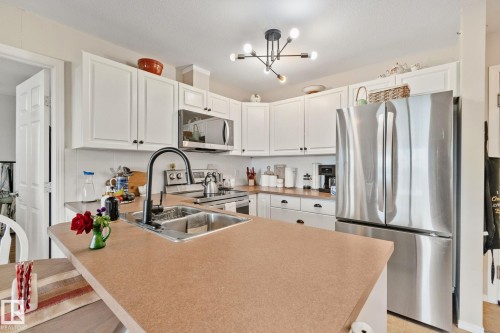 Kitchen featuring white cabinetry, stainless steel appliances, a double basin sink with a gooseneck faucet, and a contemporary chandelier - #407 4309 33 St, Stony Plain, AB - Indoor Photo Showing Kitchen With Double Sink With Upgraded Kitchen