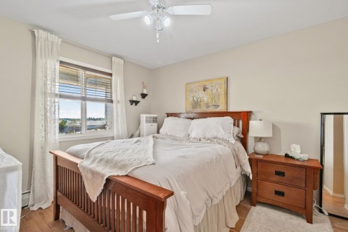 Window with horizontal blinds and lace curtains, wood-finish flooring, ceiling fan with integrated lighting, neutral wall paint, and a built-in window frame - #407 4309 33 St, Stony Plain, AB - Indoor Photo Showing Bedroom