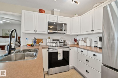 Kitchen featuring white cabinetry with black hardware, stainless steel appliances, laminate countertops, and a stainless steel sink with a black faucet - #407 4309 33 St, Stony Plain, AB - Indoor Photo Showing Kitchen With Double Sink With Upgraded Kitchen